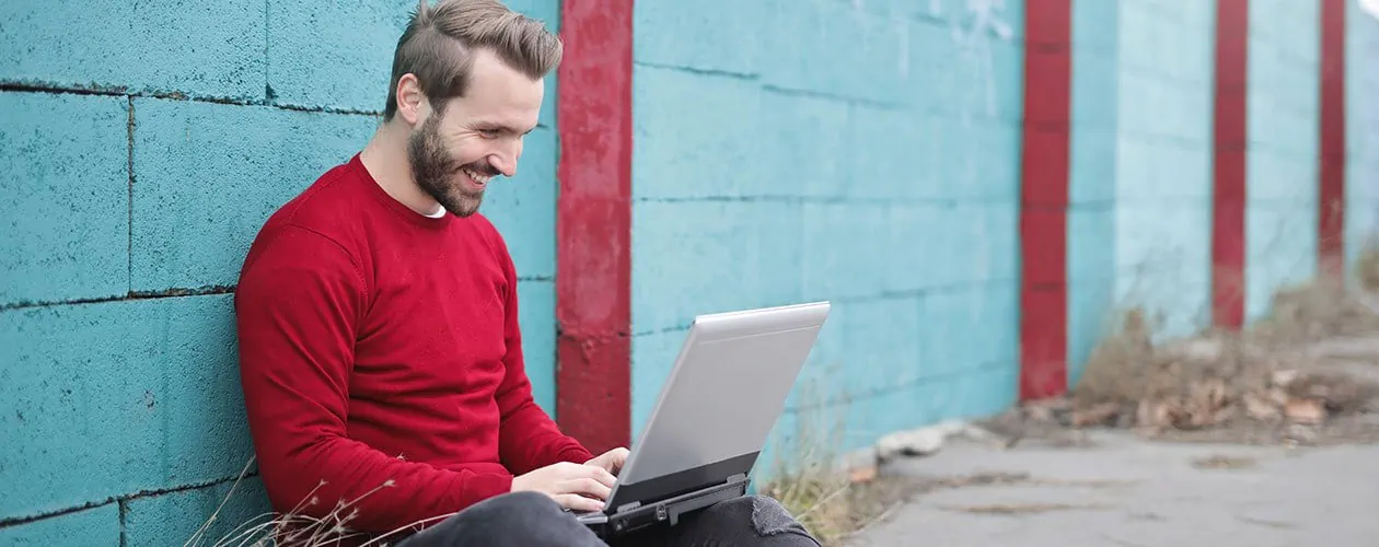 man sitting with laptop on the ground next to a wall