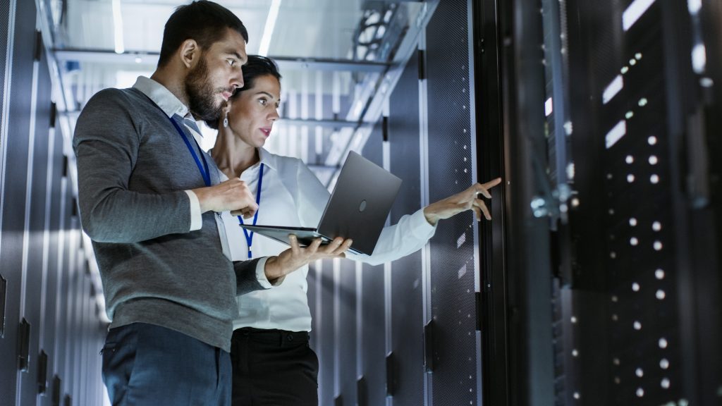 Woman and man with laptop stand in front of servers in a data center